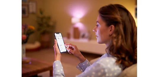 אישה שולטת בתאורה חכמה צבעונית Philips Smart LED מהאפליקציה בטלפון הנייד